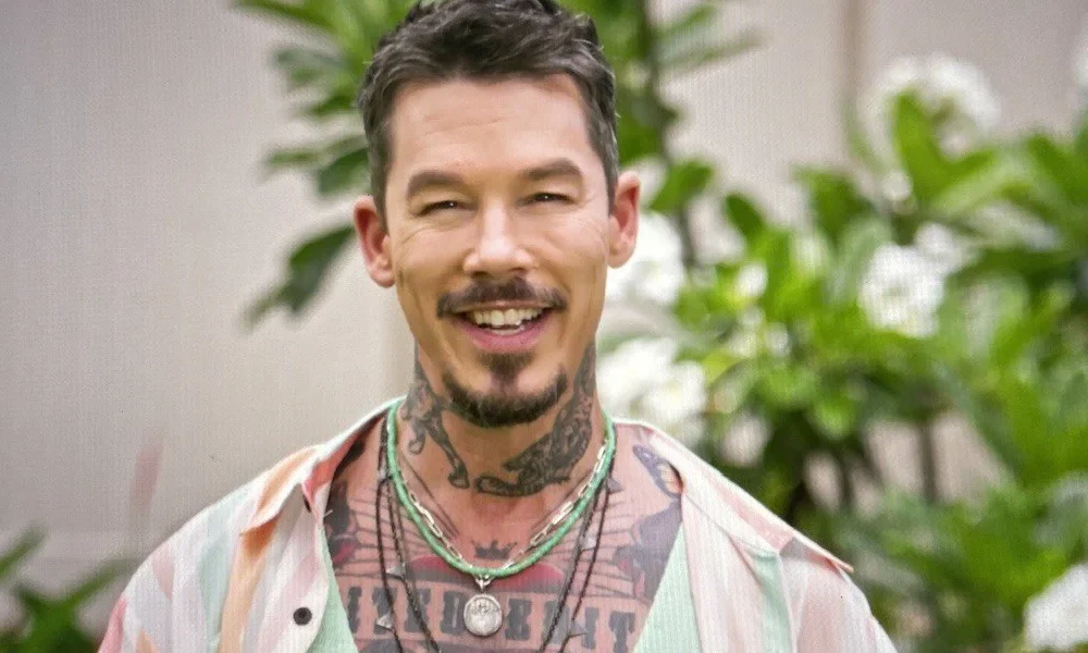 David Bromstad smiling outdoors, wearing a colorful shirt, showcasing his signature tattoos and warm personality.