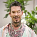 David Bromstad smiling outdoors, wearing a colorful shirt, showcasing his signature tattoos and warm personality.